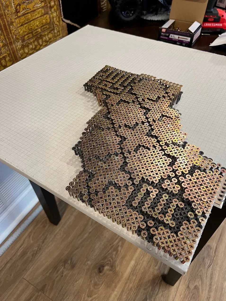 A large mosaic of brass and black screws, half finished, on a gridded white board